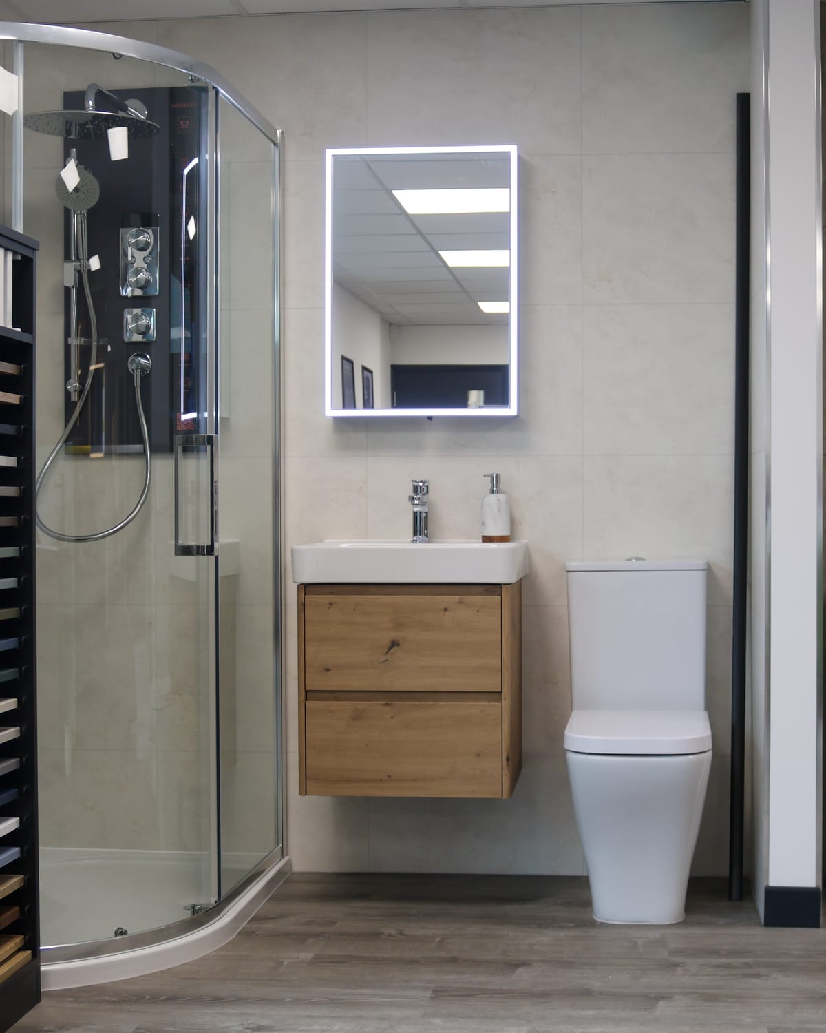 Quadrant shower enclosure, oak vanity unit with LED mirror and close-coupled toilet beside a Zaneti display at Pochin Eastbourne