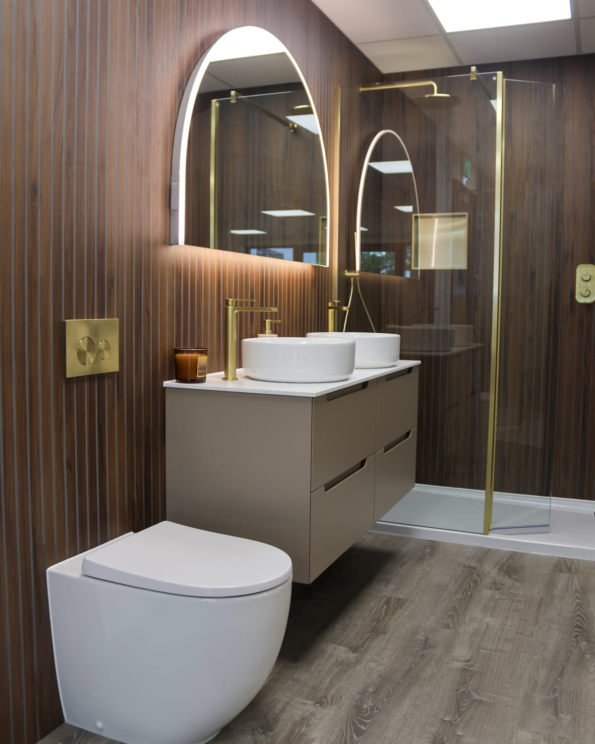 Fluted walnut wall with arched LED mirror, brass taps, twin countertop basins and walk-in shower at Pochin Eastbourne