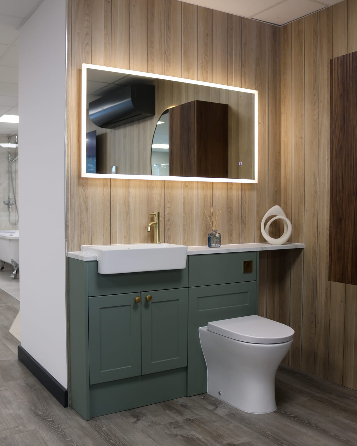 Sage green fitted furniture with semi-recessed basin, brushed brass tap and LED mirror on wood panelling at Pochin Eastbourne